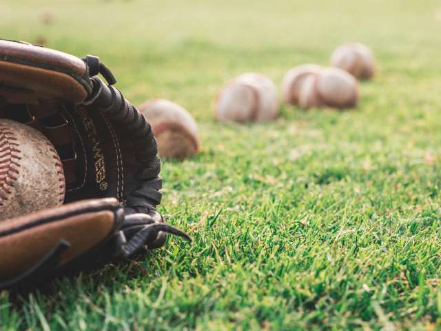 A baseball glove and a number of baseballs lay on a grassy field.