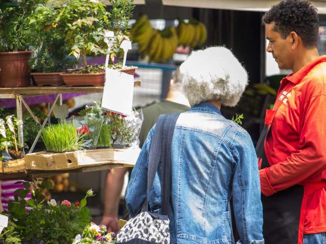 A woman talks to a worker at a produce stand. 