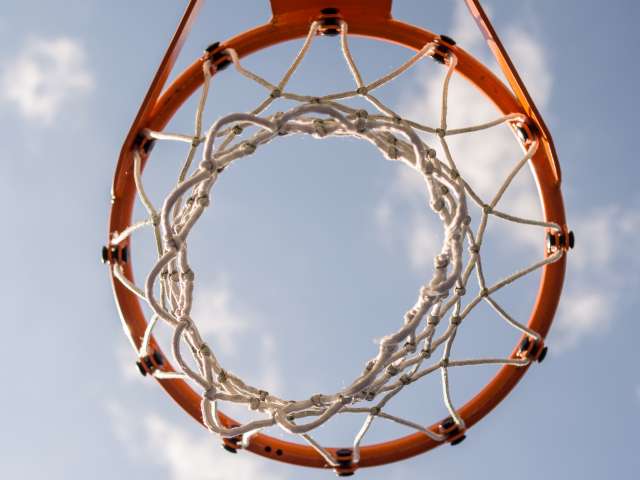 The netting of a basketball hoop as seen from the ground up toward the sky.