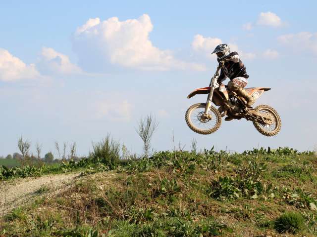 A man rides over a grassy hill on a motorbike. 