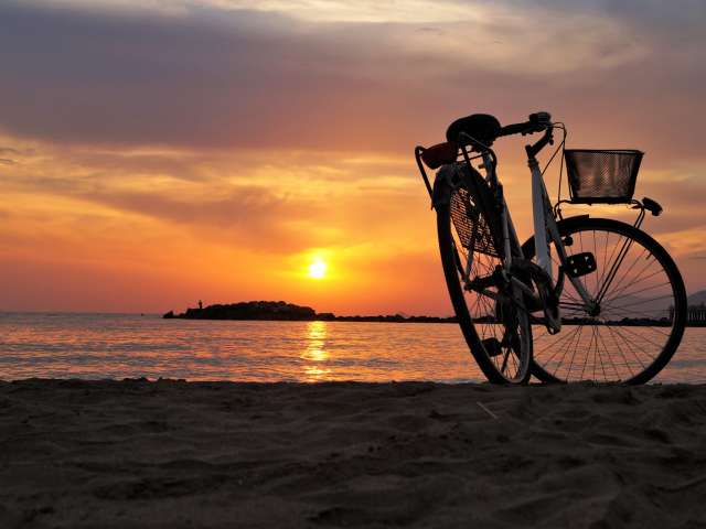 A bicycle parked on the beach at sunset.