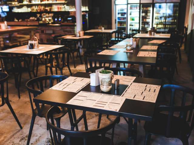 The inside of a homestyle restaurant with wooden chairs and multiple tables, covered with paper menus.