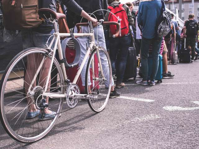 People stand in a long line on a paved surface. One person holds a road bike.