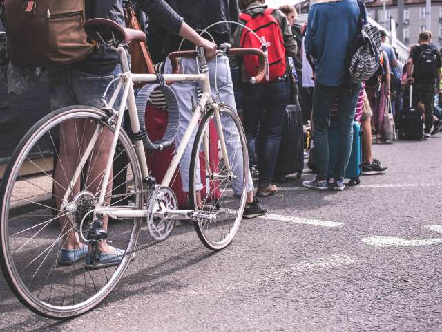 People stand in a long line on a paved surface. One person holds a road bike. 