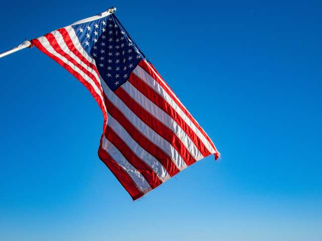 A crisp and colorful American flag waves in a breeze on a clear blue day.