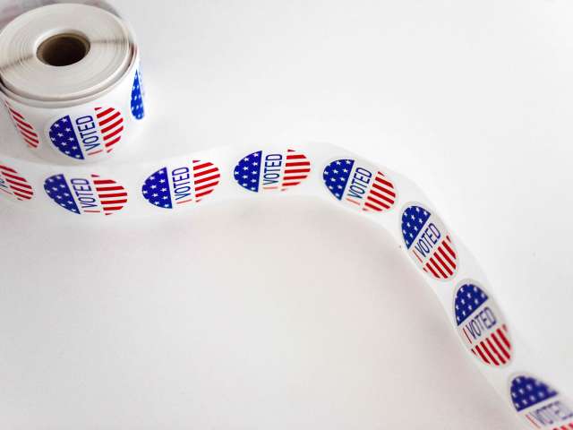 A roll of I VOTED stickers unravels on a white table top.