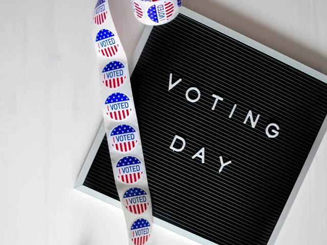 A black board with the words, Voting Day, in white letters as well as a roll of voting stickers. 