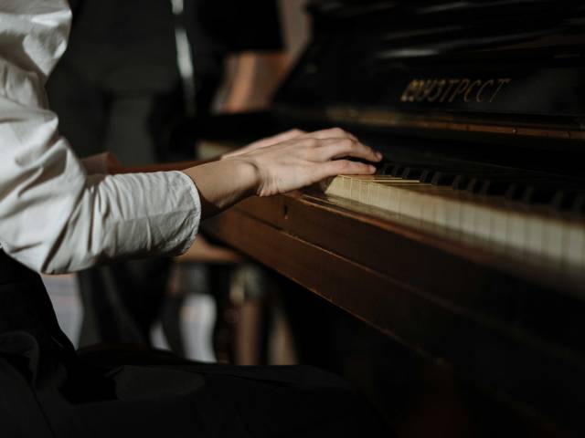 A woman with a white shirt sits at an old piano and plays.