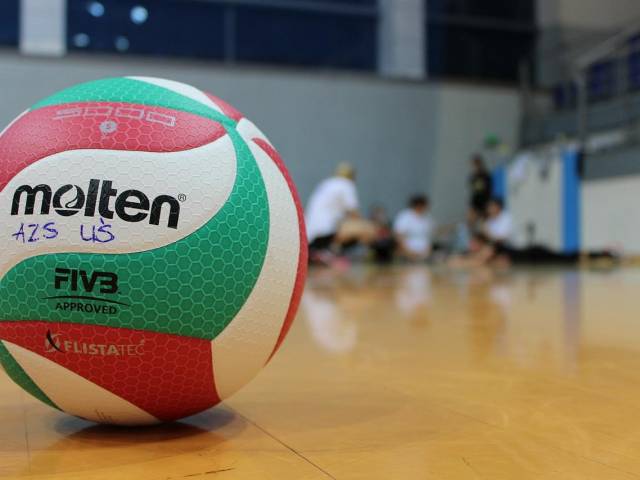 A white, green, and red volleyball sits on a shiny volleyball court.