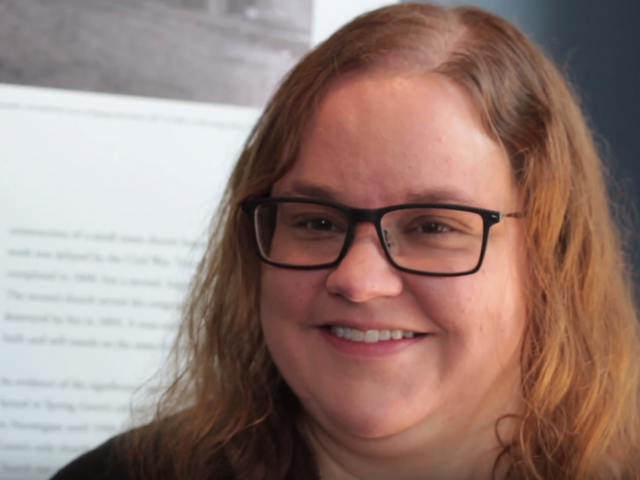 With shoulder-length red hair and black-rimmed glasses, Sarah Schroeder smiles at the camera.