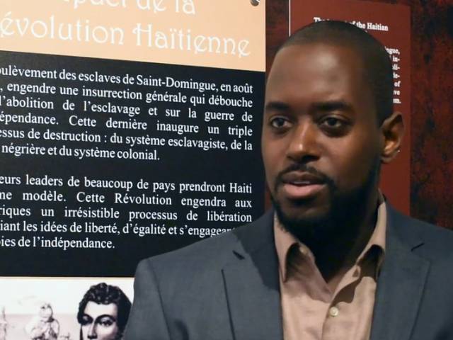 Pedro, wearing a gray suit jacket and beige collared shirt, sits and chats with an interviewer. 
