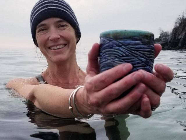 A woman with a swim cap on raises her hands out of the water and holds a cup in her hands. 