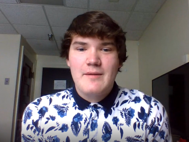 Reeve has short brown hair and a collared shirt, with blue flowers and patterns on it.