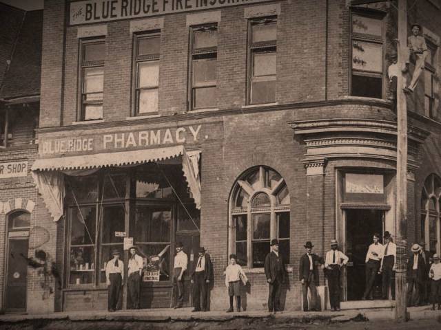 Vintage photo of a pharmacy in the early 20th as people stand on the corner and wait outside.