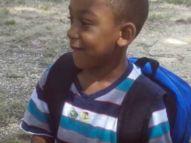 A young boy named Michael smiles and wears a blue backpack and blue striped shirt.