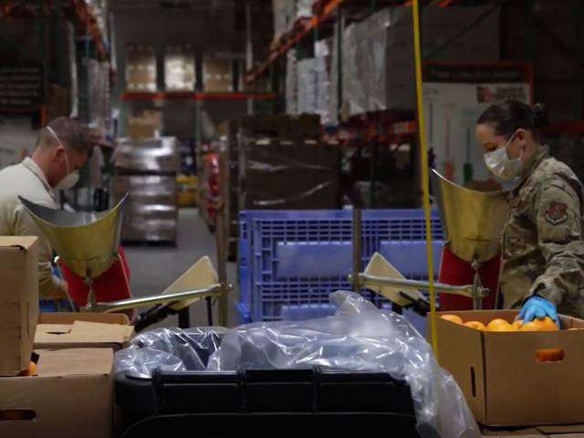 Two people wearing army fatigues load supplies in boxes in a warehouse.