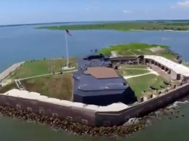 A stone and brick fort shaped like a pentagon sits in the middle of a waterway. 