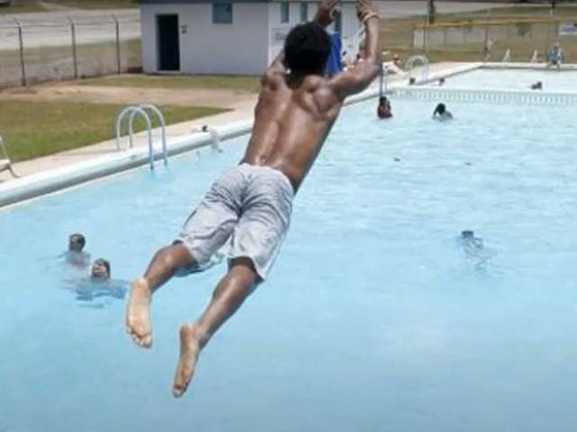 A boy with gray swim trunks does a dive into a pool.