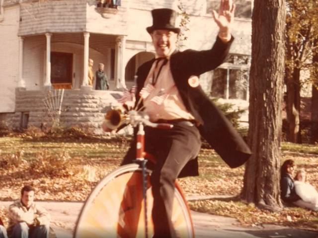 A man in a top hat rides a unicycle in a vintage photo.