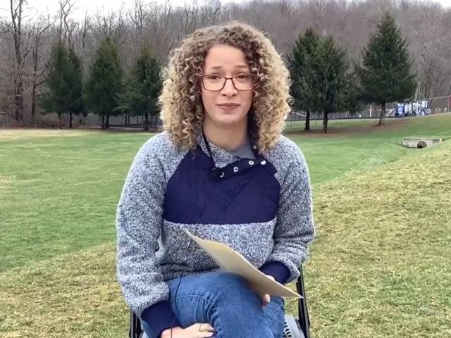 A woman curly hair and a blue sweater sits in a chair in a field.
