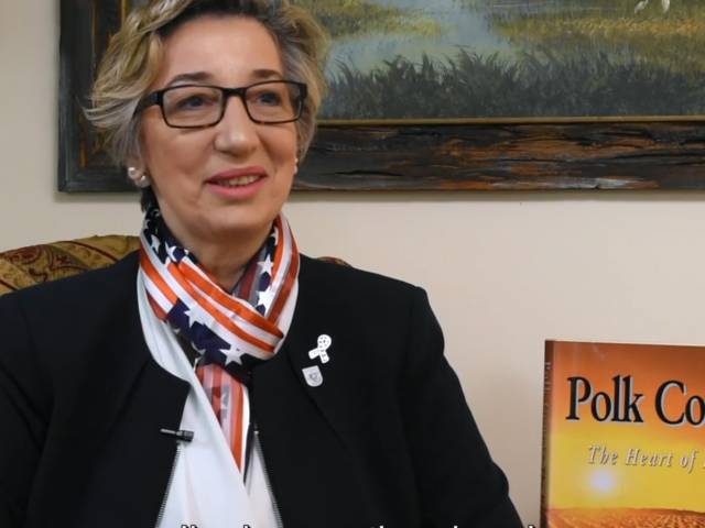 A woman with short gray hair wears eyeglasses and an American flag scarf.