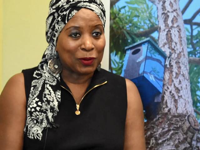 A woman with a black top wears a black and white head scarf in a library setting. 