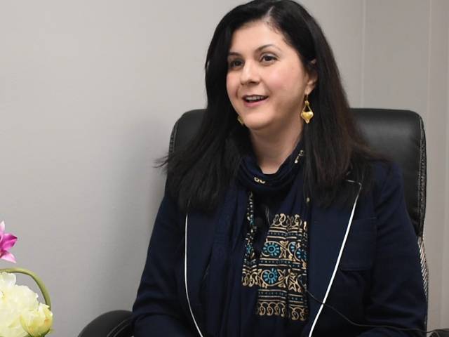 A woman with black hair sits in a leather chair beside some flowers.