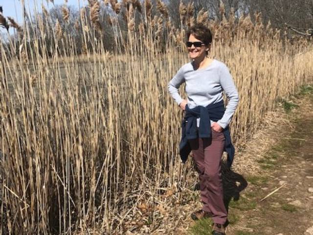 A woman with brown and sunglasses walks in a salt marsh.