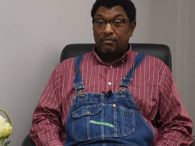 Jimmy wears a red, plaid shirt and blue jean overalls.