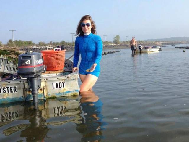 Abigail wears a blue wetsuit and stands in the water next to a small boat.