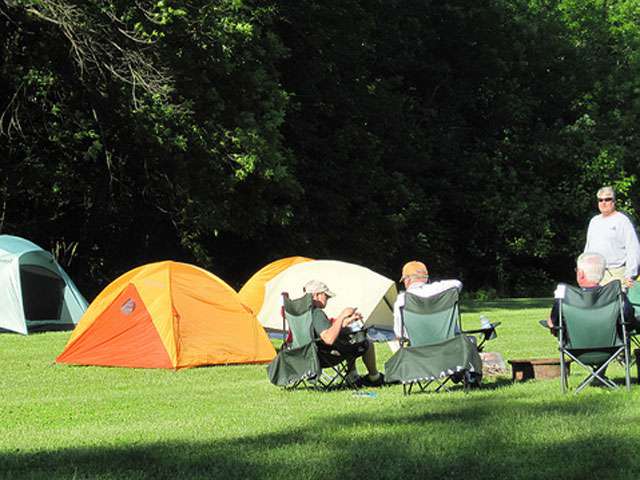 A group of campers sit outside of their colorful tents.