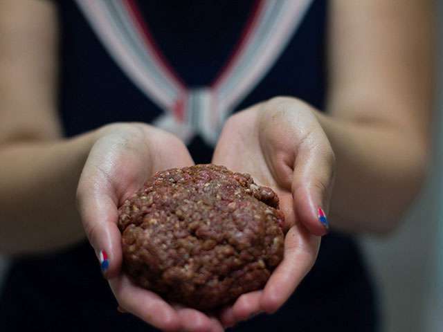 A woman holds a ball of ground beef.