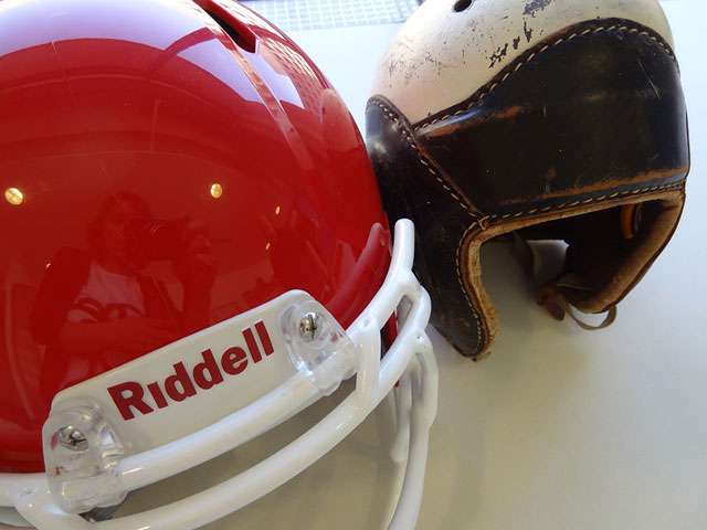 A bright red, modern football helmet positioned next to an antique leather football helmet. Photo by Heather Shelton