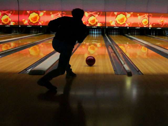 The back of a person releasing a ball at a bowling alley. 