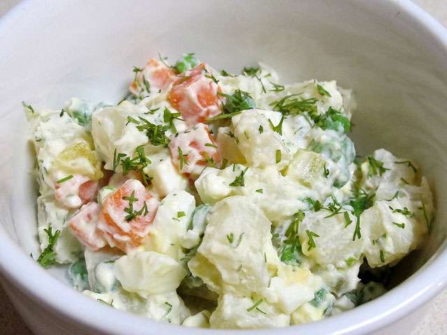 A white bowl filled with a creamy potato salad dish. 