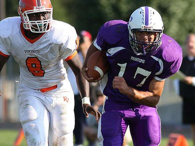 High School football players run down the field as opponents. 