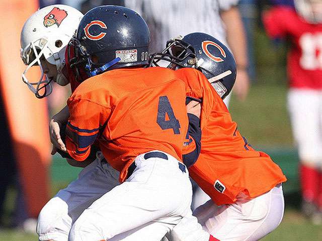 Pee-wee football players run down in the field in orange jerseys. 