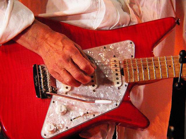 A detail of a man holding a bright red electric guitar.