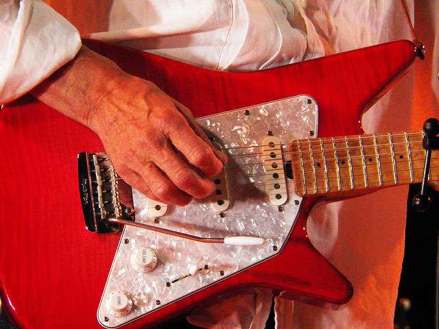 A detail of a man holding a bright red electric guitar. 