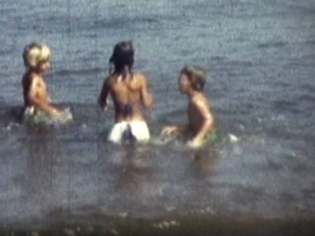 Three young children splash in the water in a vintage photo.