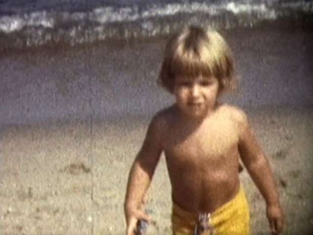 A boy with blonde hair walks along the beach in a vintage video clips.