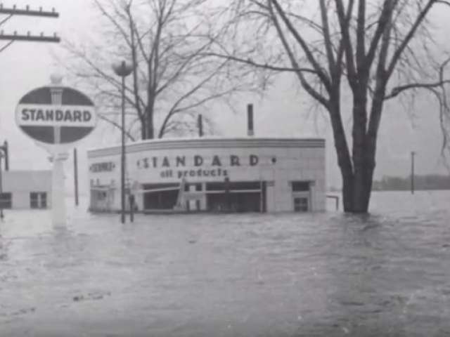 A vintage photo of a gas station that is flooded up to the tops of the windows. 