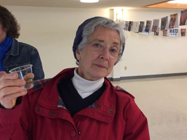 A woman stands holding up a glass of tap water.