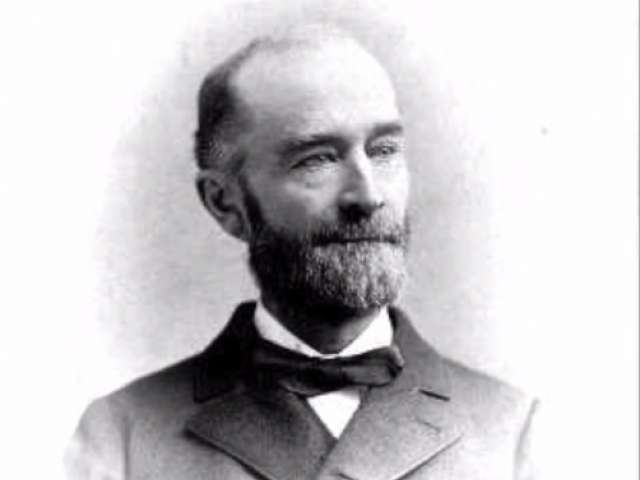 Historic photo of a man with a beard and an overjacket with black bowtie. 