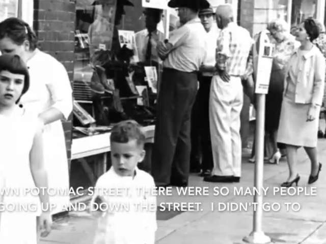 People in up-scale attire walk down the sidewalk and look into store windows in a vintage photo of a small-town Saturday night.