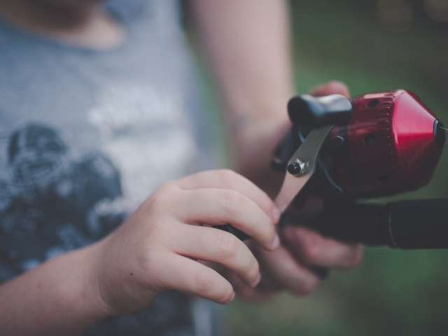 A girl holds a fishing rod as someone leans down to help. 