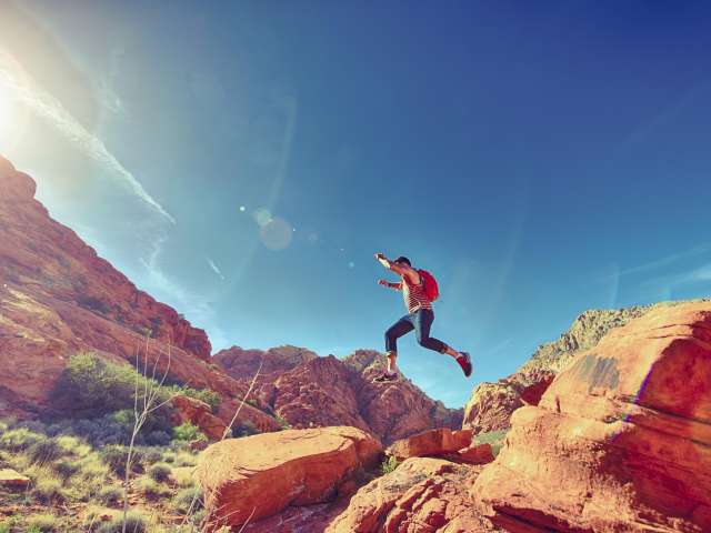 A person jumps across red rocks in a desert landscape.