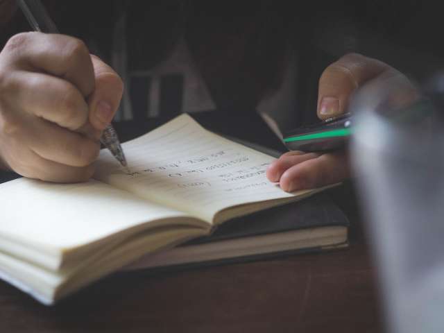 A student writes in a small notebook. Pixabay stock photo