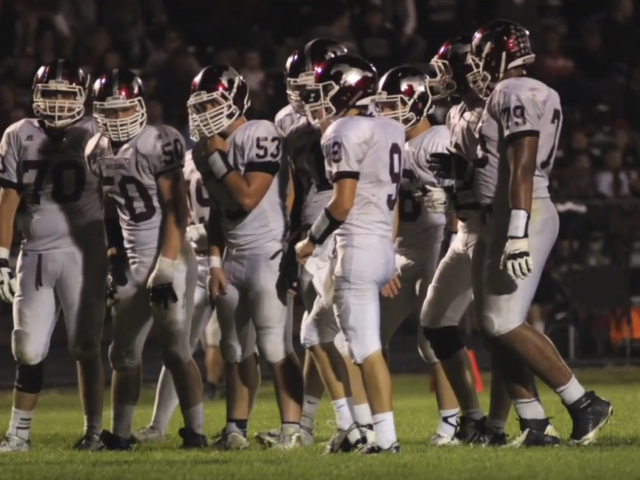 A football team huddles together to talk right before or after a play on the field during a game. 