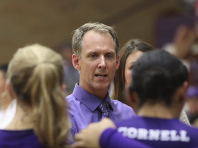 Wearing a blue shirt, coach Jeff Meeker talks to volleyball player's during a game. 
